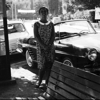 Woman stands beside vintage car in black and white photograph.