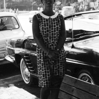 Woman stands beside vintage car in black and white photograph.
