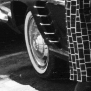Woman stands beside vintage car in black and white photograph.