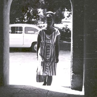 Person stands in an archway, viewed from a dark interior.