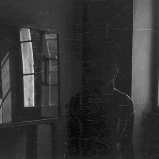 Man stands in shadow, facing a window with light.