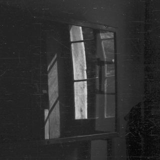 Man stands in shadow, facing a window with light.