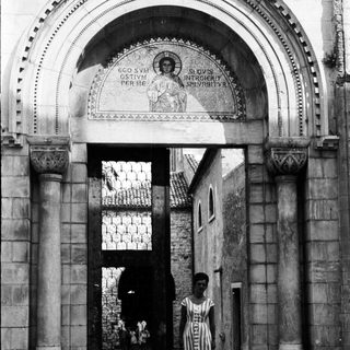 Woman walks through a monumental, arched doorway.