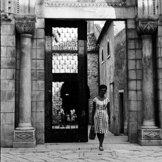 Woman walks through a monumental, arched doorway.