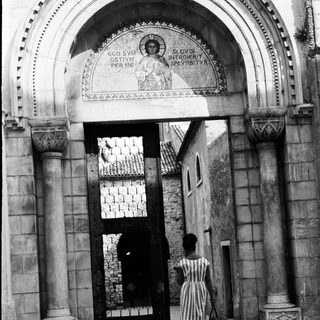 Woman walks through an arched doorway with mosaic.