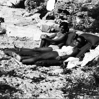 People relax on rocky shoreline with ocean backdrop.