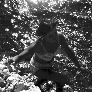 Woman climbing rocks in water, black and white photo.