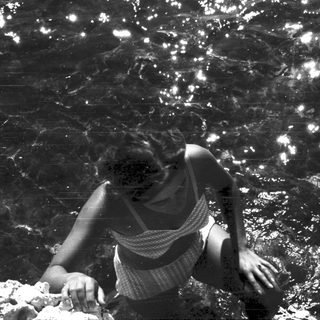 Person in swimwear emerging from water, sunlight sparkling.