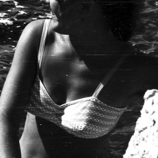 Woman in swimwear stands near rocks overlooking the ocean.