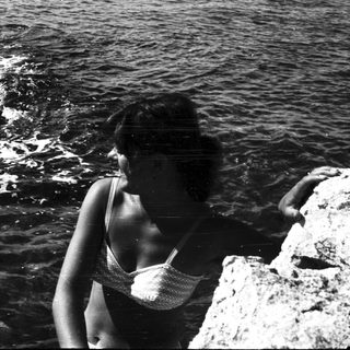 Woman in swimwear stands near rocks overlooking the ocean.