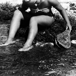 Woman sits by water, holding a turtle.