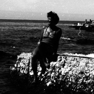 Person sits on rocks overlooking a dark body of water.