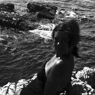 Woman sits on rocks near the water's edge.