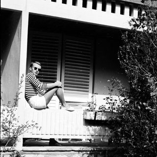 Man in sunglasses sits on a ledge, outdoors.