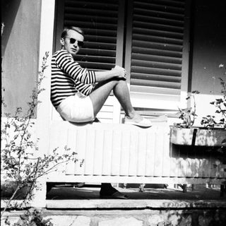 Man in sunglasses sits on a ledge, outdoors.