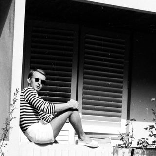 Man in sunglasses sits on a ledge, outdoors.