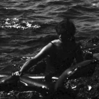 Black and white photo of figures on rocks in ocean.