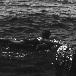 Person swimming near rocky coastline in a dark sea.