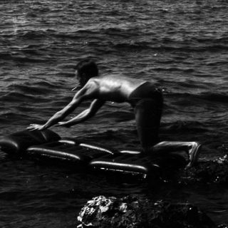 A shirtless person balances on a float in the ocean.