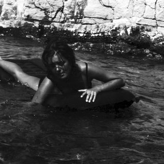 Woman submerged in water, rocky background visible.