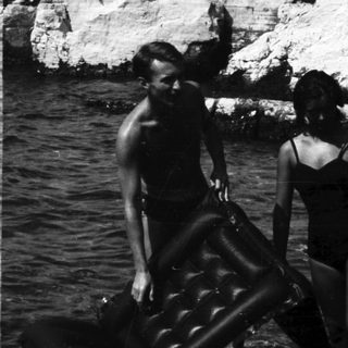 Two people carry an inflatable raft in shallow water.