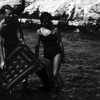 Two people carry an inflatable raft in shallow water.