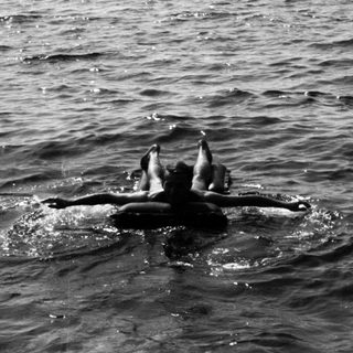 Here's a brief summary of the image: Person swimming in ocean, another person on rocks nearby.