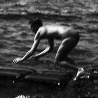 Man leaps from rocks into ocean during black and white photograph.