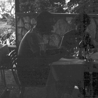 Two figures seated at a table in a dark setting.
