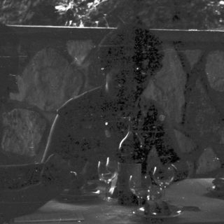 Two figures seated at a table in a dark setting.