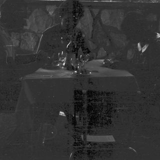 Two figures seated at a table in a dark setting.