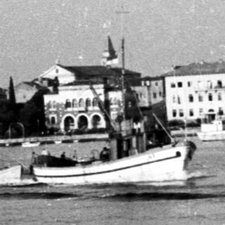 Several boats are on water with buildings in background.