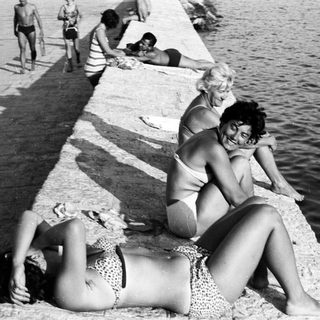 People sunbathing and relaxing on a concrete seaside wall.