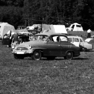Black and white image of a vintage campsite with vehicles.