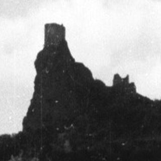 Ruined castle sits atop a wooded hill, viewed from below.