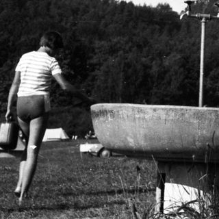 Person drinks from a fountain in an outdoor setting.