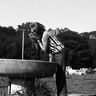 Person drinks from a fountain in an outdoor setting.