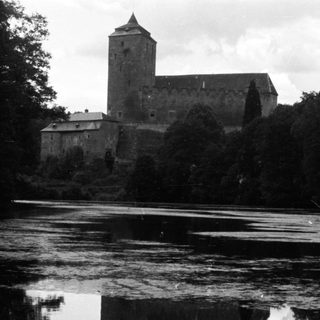 Castle reflected in water, surrounded by trees.