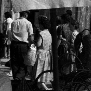 Black and white photo depicts people at a market stall.