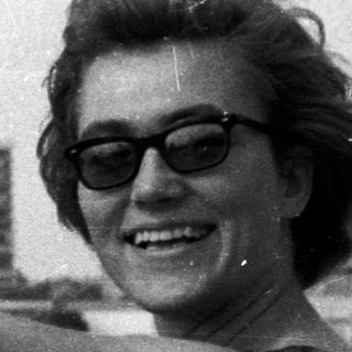 Woman smiles, pointing towards cityscape reflected in water.