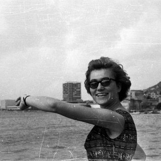 Woman smiles, pointing towards cityscape reflected in water.