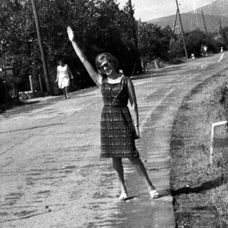 Woman waving on a rural road in a vintage scene.