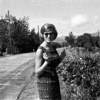 Woman in a dress stands on a rural road.