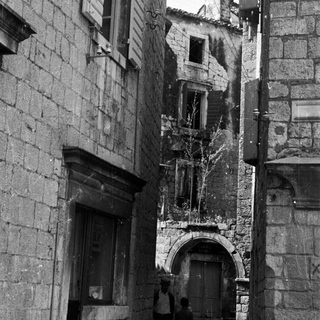 Two figures stand in a narrow, old stone alleyway.