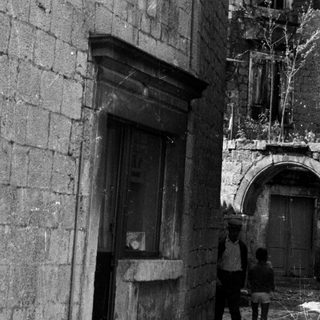 Two figures stand in a narrow, old stone alleyway.