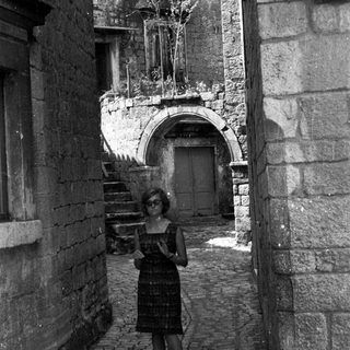 Woman stands in a narrow, old stone alleyway.