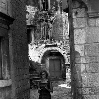 Woman stands in a narrow, old stone alleyway.