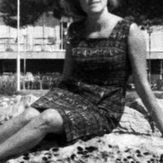 Woman sits on rocks overlooking the water and building.