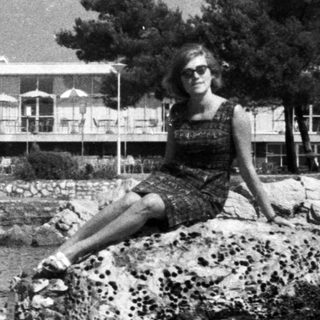Woman sits on rocks overlooking the water and building.