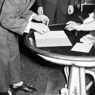 Man signing a document, flanked by two men.